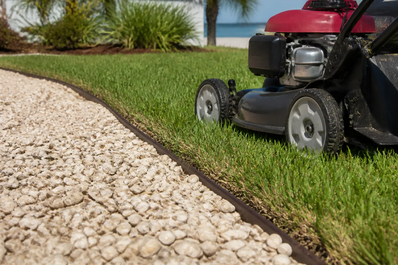 Lawn Mower Beside a Shell Aggregate Border A red and black lawn mower on green grass beside a pale shell aggregate bed separated by curved dark edging.; coquina shell next to lawn mower planning guide