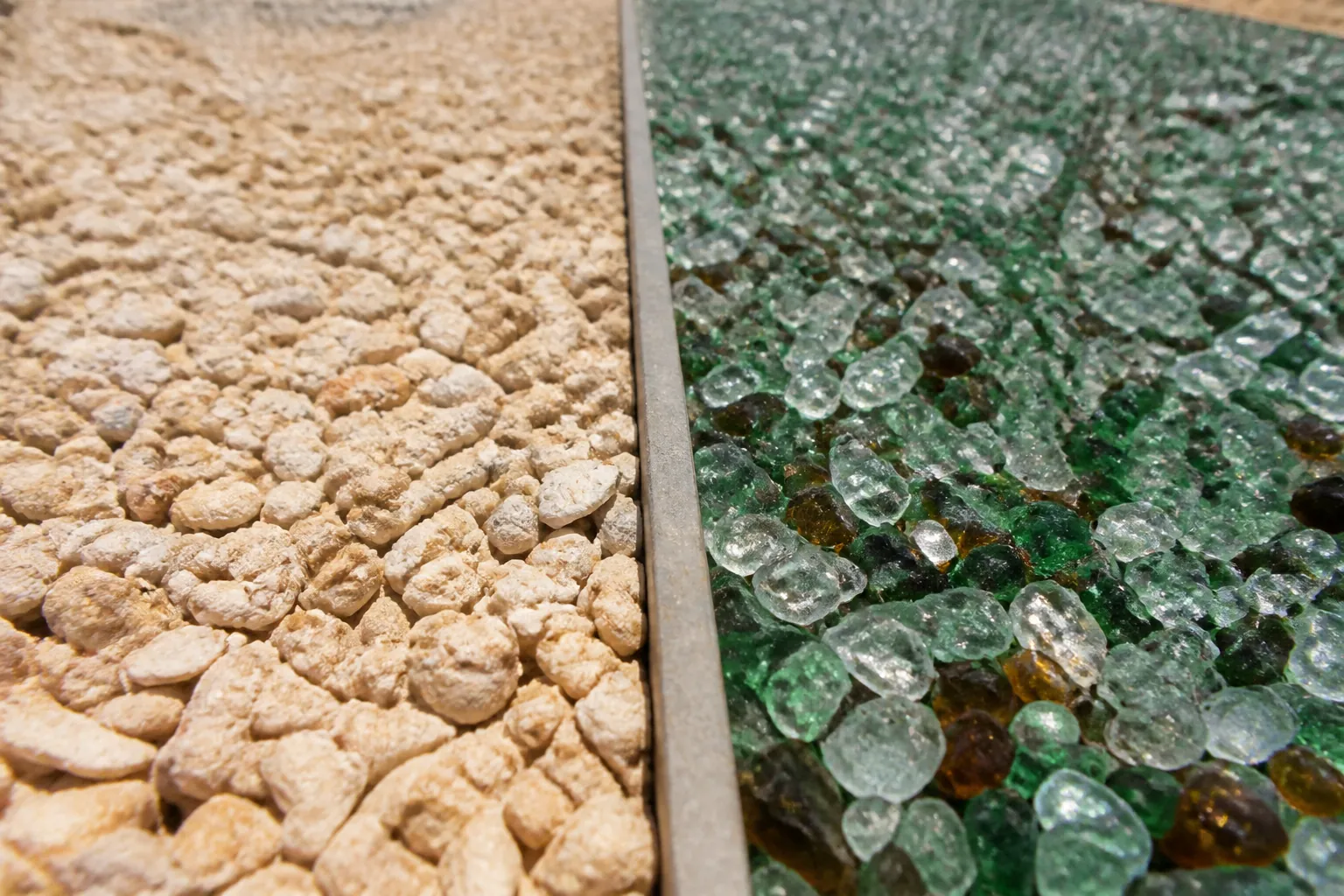 Coquina Shell and Recycled Glass Side by Side Beige coquina shell aggregate on the left and green, clear, and amber glass pieces on the right, separated by a divider.